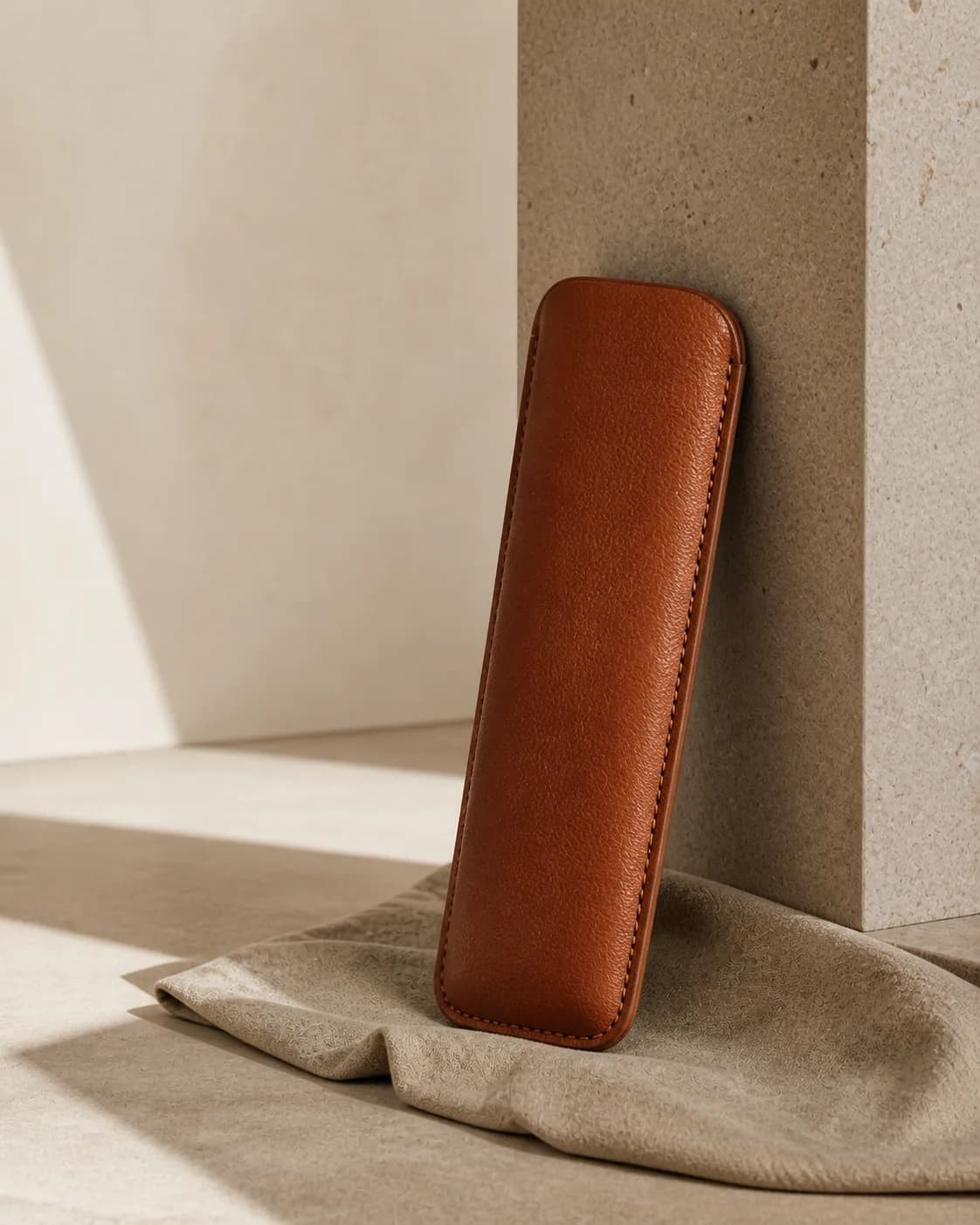 Slim rounded chestnut leather case in a warm minimal studio.